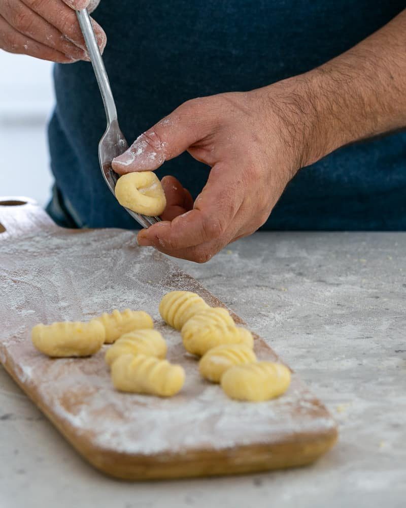 Rolling gnocchi dough balls over a fork to make restaurant style ricotta gnocchi's with tomatoes and olives