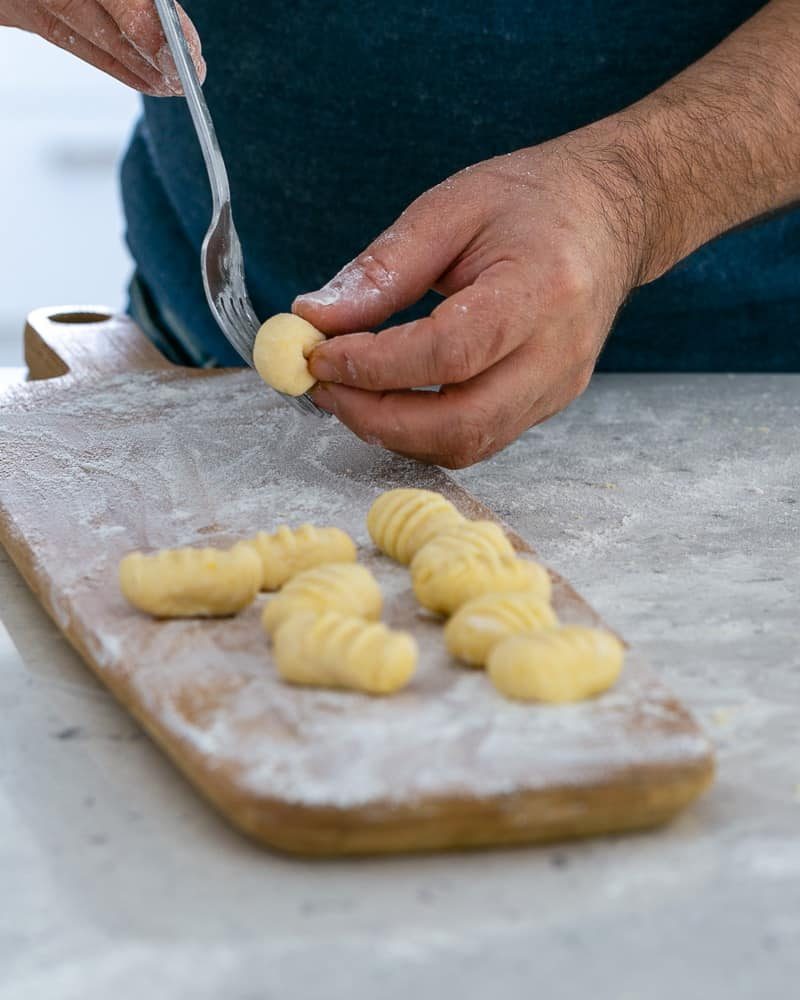 Rolling gnocchi dough balls over a fork to make restaurant style ricotta gnocchi's with tomatoes and olives