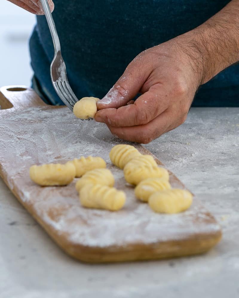 Rolling gnocchi dough balls over a fork to make restaurant style ricotta gnocchi's with tomatoes and olives