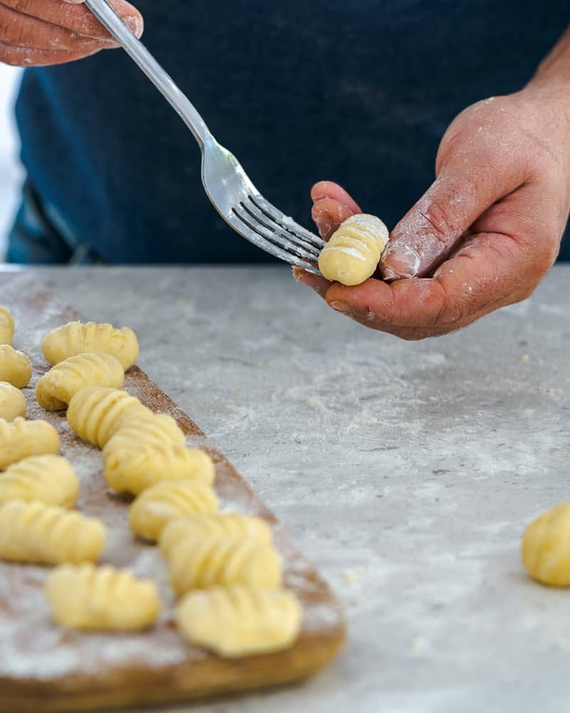 Rolling gnocchi dough balls over a fork to make restaurant style ricotta gnocchi's with tomatoes and olives