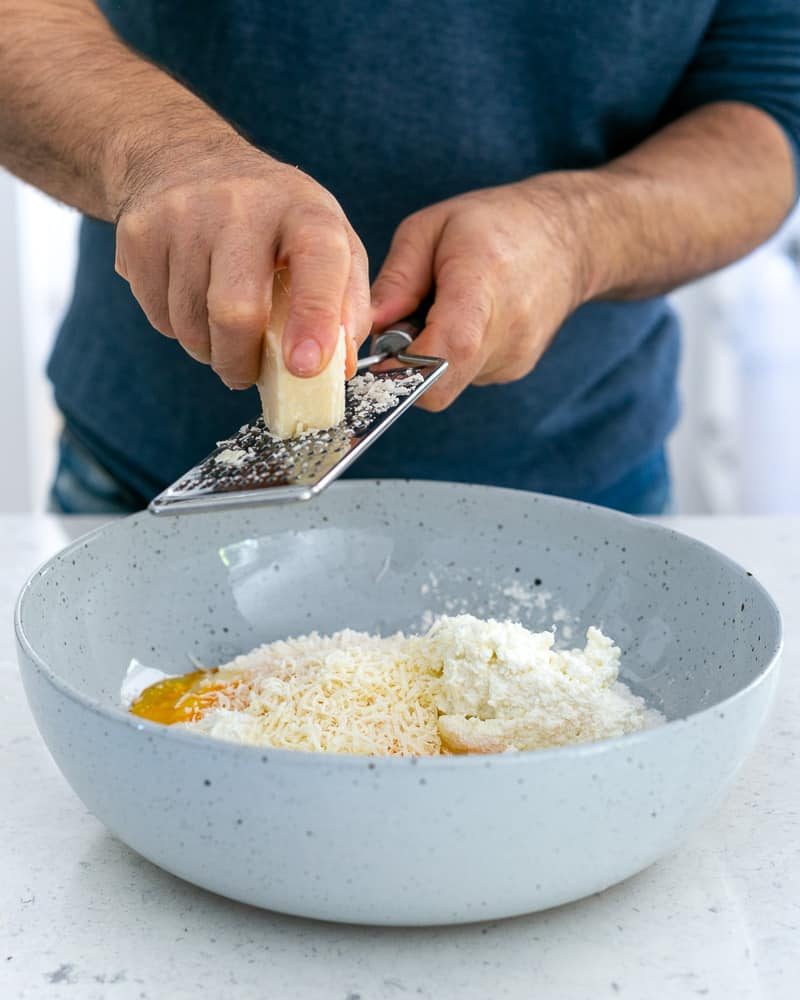Adding parmesan cheese to eggs, flour and ricotta in a bowl 