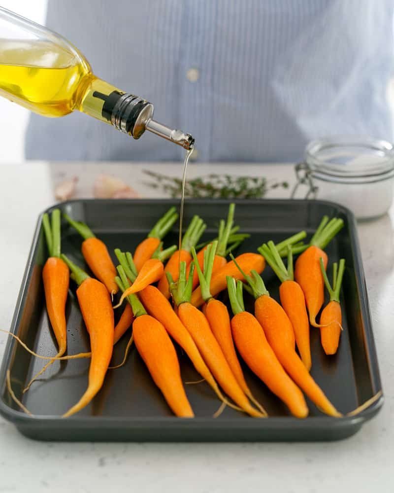 Olive oil drizzled over peeled baby carrots for oven baked baby carrots with chimichurri