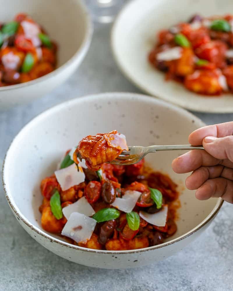 Gnocchi on a fork over a bowl of ricotta Gnocchi's with tomatoes and olives