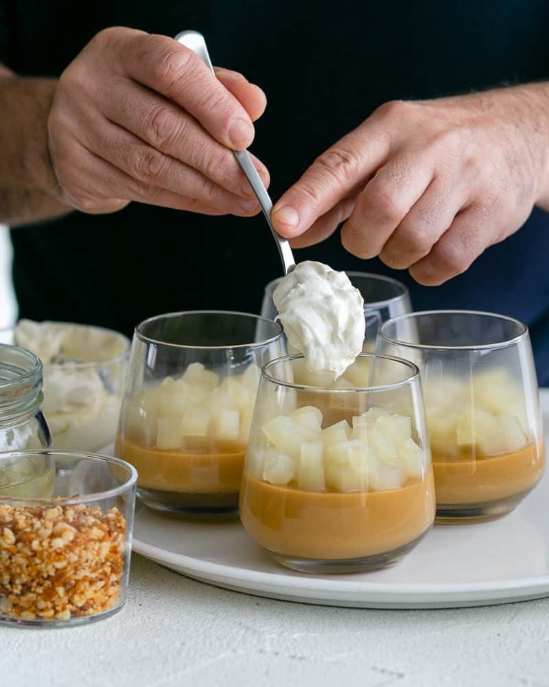 Adding whipped cream on top of diced pears on the set caramel petit pots