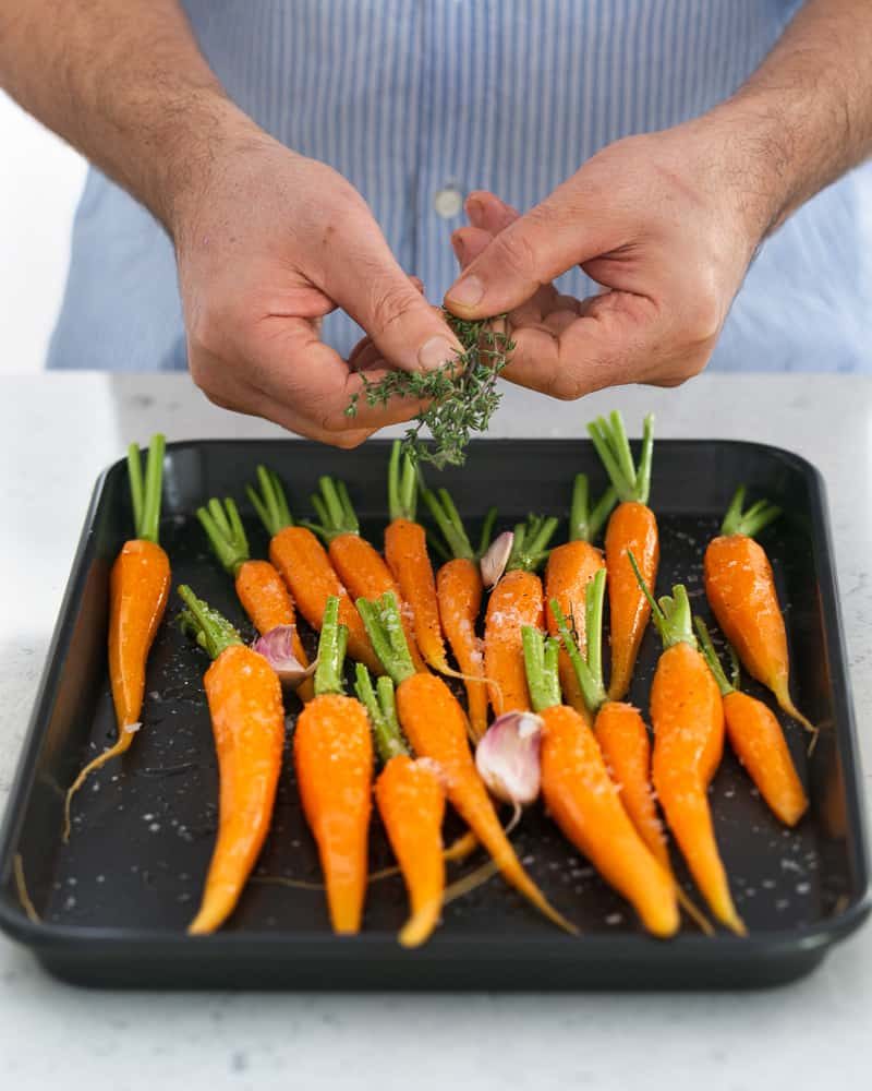 Sprinkling fresh thyme on baby carrots on baking tray