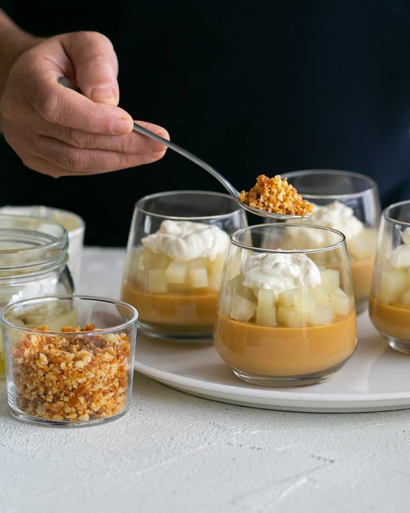 Final topping of Macadamia Brittle crumble on top of the whipped cream on the caramel petit pots with poached pears