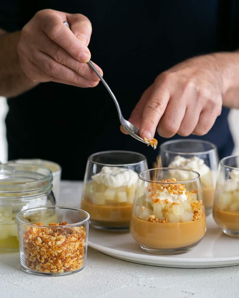 Sprinkle of Macadamia Brittle crumble on top of the whipped cream on caramel petit pots with poached pears