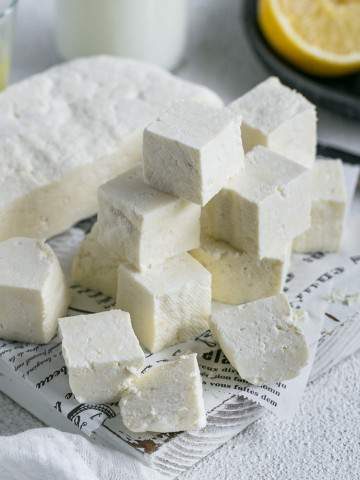 Paneer cut in cubes with half the paneer slab along with lemon juice and milk in background for How to make paneer