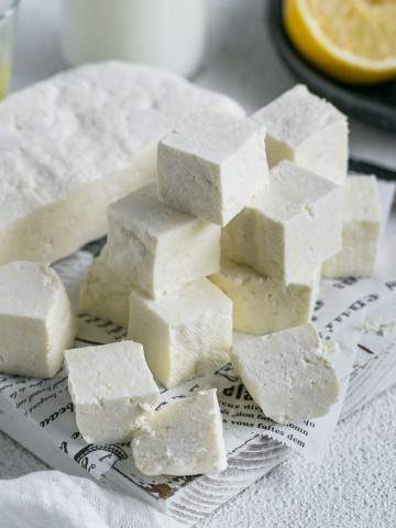 Paneer cut in cubes with half the paneer slab along with lemon juice and milk in background for How to make paneer