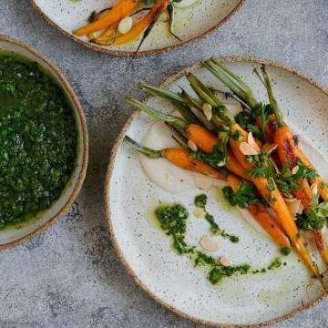 Oven roasted baby carrots with chimichurri beautifully arranged on a ceramic plate