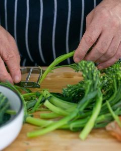 Peeling broccolini stem with a peeler for Casarecce Pasta with Asparagus, Kale and Garlic dish