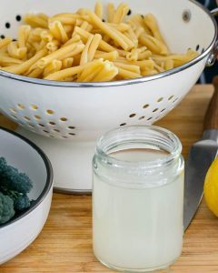 Pasta cooking water in a jar with cooked pasta in a strainer in the background