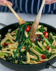 Tossing Casarecce Pasta with Asparagus, Kale and Garlic with two wooden spoons in the pan