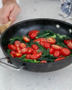 Cut red tomatoes in hot pan with kale, broccolini and asparagus