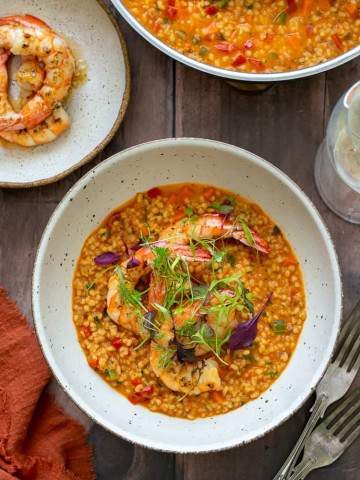 Garlic roasted prawns with fregola sarda individually plated in a bowl garnished with prawns and herbs