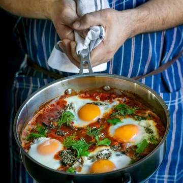 Chef showing freshly cooked Kale Shakshuka with Chickpeas and zataar in a pan