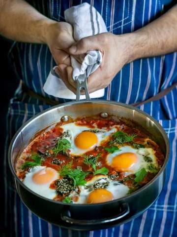 Chef showing freshly cooked Kale Shakshuka with Chickpeas and zataar in a pan