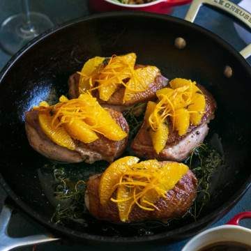 Prepared duck breasts in an iron skillet, topped with orange segments, orange zest julienne and thyme