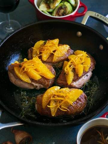 Prepared duck breasts in an iron skillet, topped with orange segments, orange zest julienne and thyme