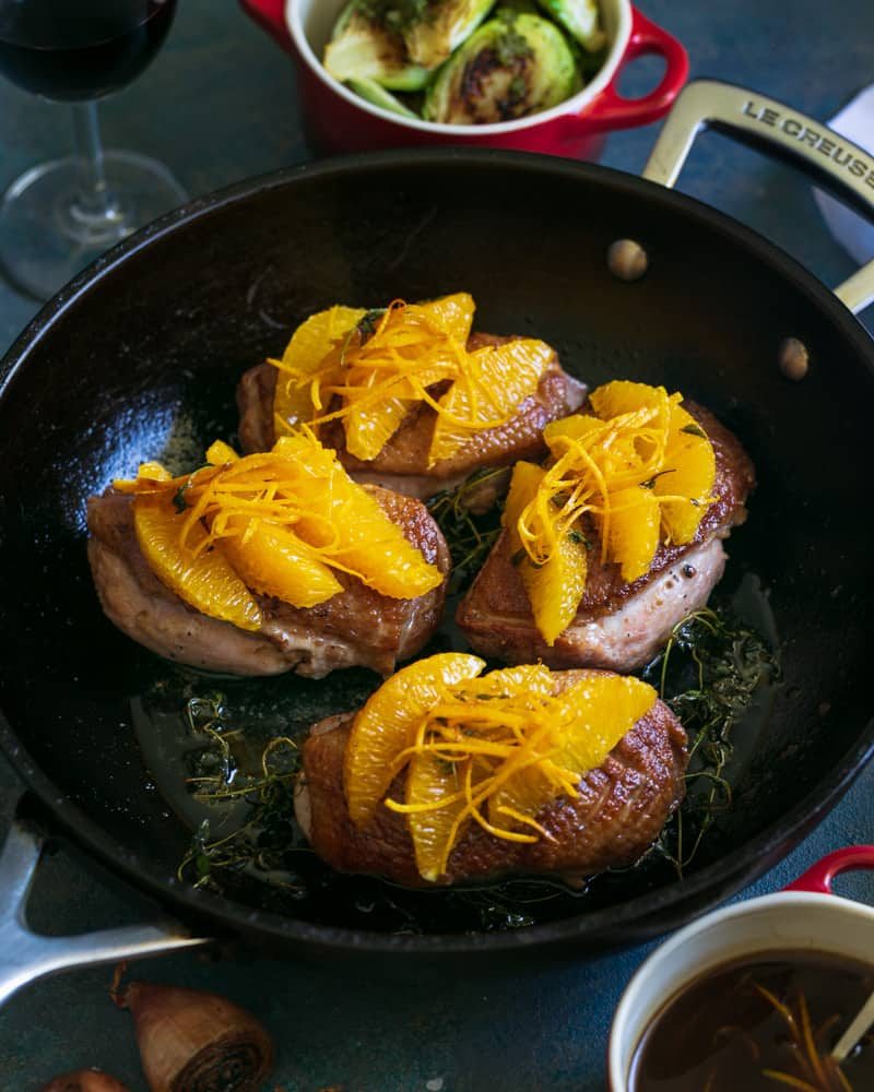 Prepared duck breasts in an iron skillet, topped with orange segments, orange zest julienne and thyme