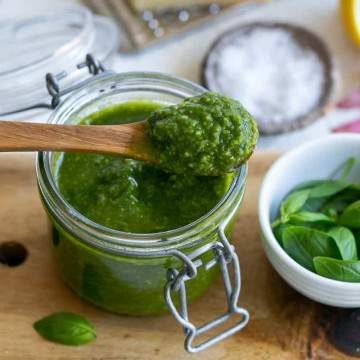 Basil pesto in a jar with a wooden spoon on top with basil pesto in it