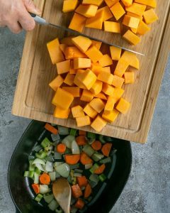 Stew pot with chopped carrots, onions, celery, chopped butternut squash cubes being added to the stew pot