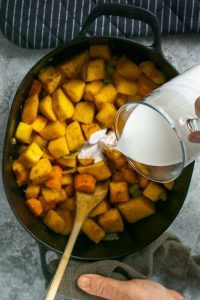 Coconut milk being added to roasted vegetables in stew pot