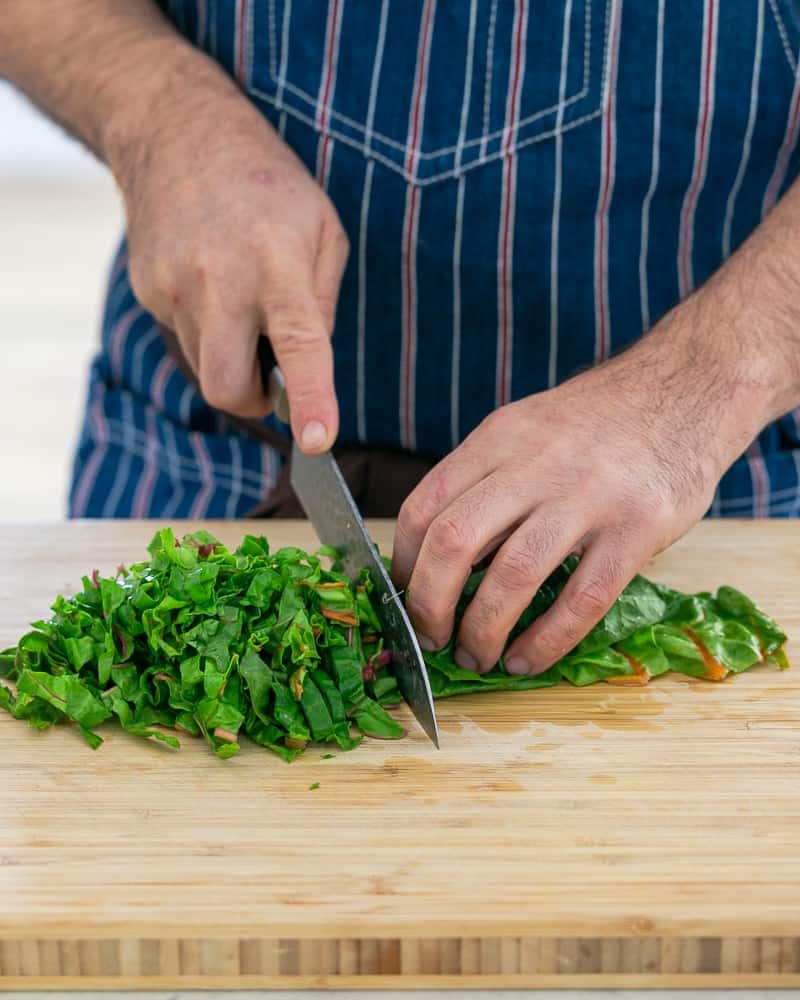 A person chopping the swiss chard leaves in stripes to make Baked sweet Potato with Lentils and Swiss Chard