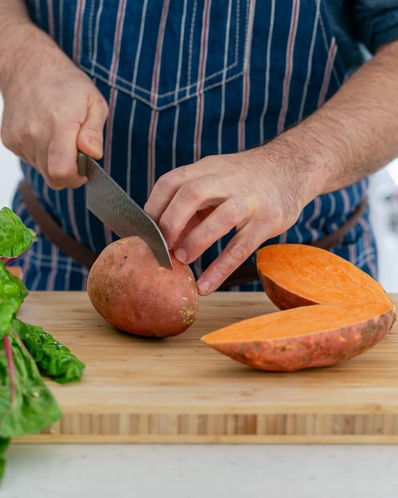 A person cutting Sweet Potato to make baked sweet potato with lentils and swiss chard