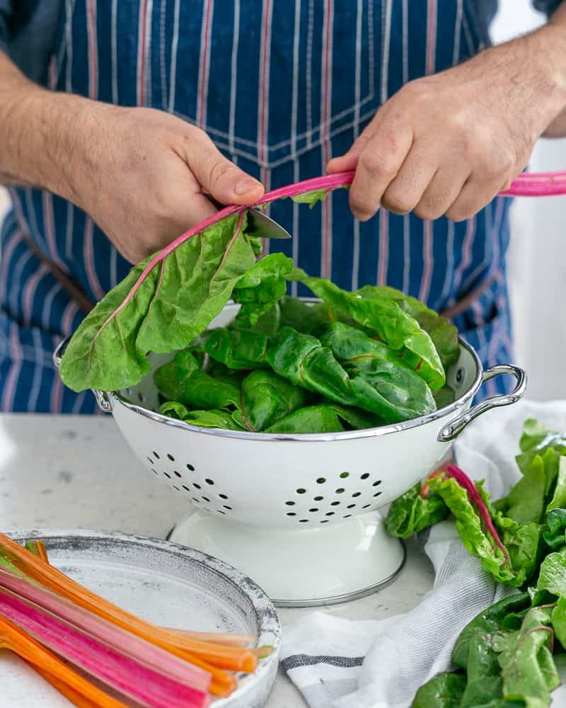 A person cutting stems of the swiss chard to make Baked sweet Potato with Lentils and Swiss Chard