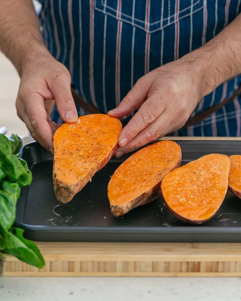 A person arranging the prepared the seasoned sweet potatoes on a baking tray to make Baked sweet Potato with Lentils and Swiss Chard