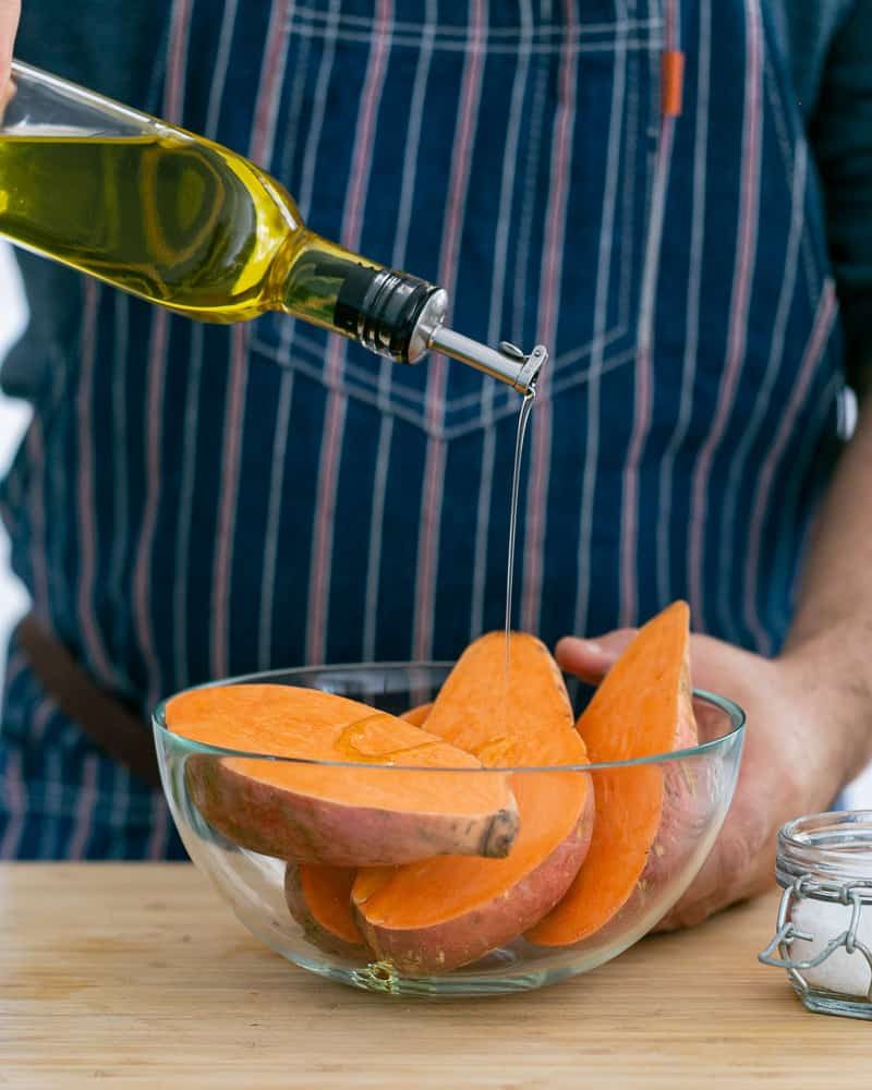 A person putting olive oil on cut Sweet Potato to make baked sweet potato with lentils and swiss chard