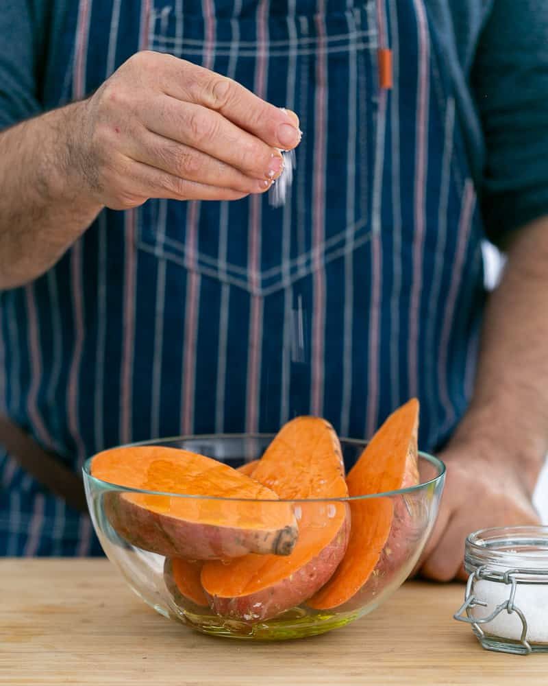 A person adding sea salt to cut sweet potatoes to make Baked sweet Potato with Lentils and Swiss Chard