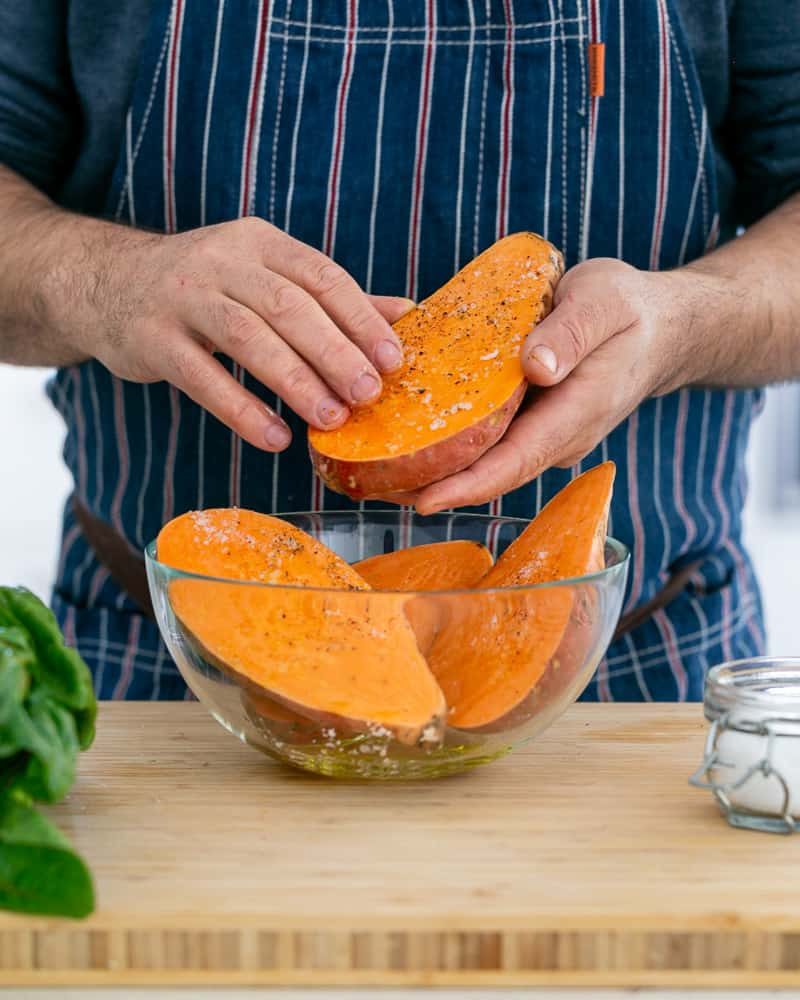 A person seasoning sweet potatoes to make Baked sweet Potato with Lentils and Swiss Chard