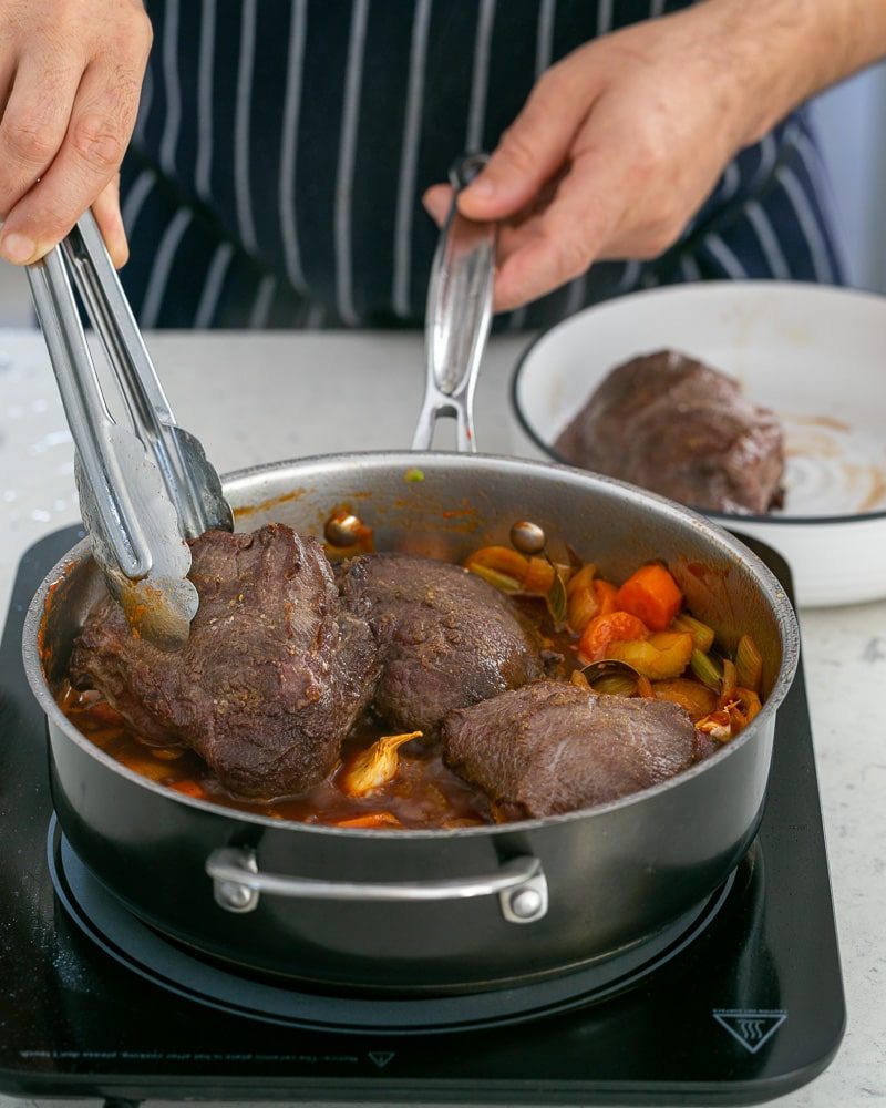 Putting beef cheeks back into the jus for braising 