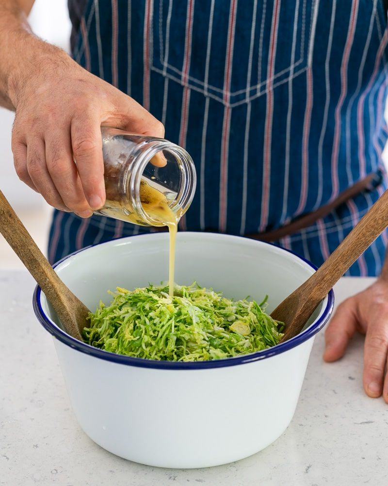 Salad dressing with raisins added to brussels sprout slaw in a bowl