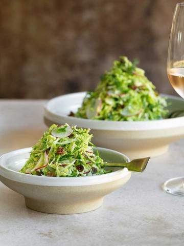 Brussels sprout slaw with raisins served in a big and small bowl with a glass of rose on the side
