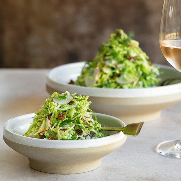 Brussels sprout slaw with raisins served in a big and small bowl with a glass of rose on the side