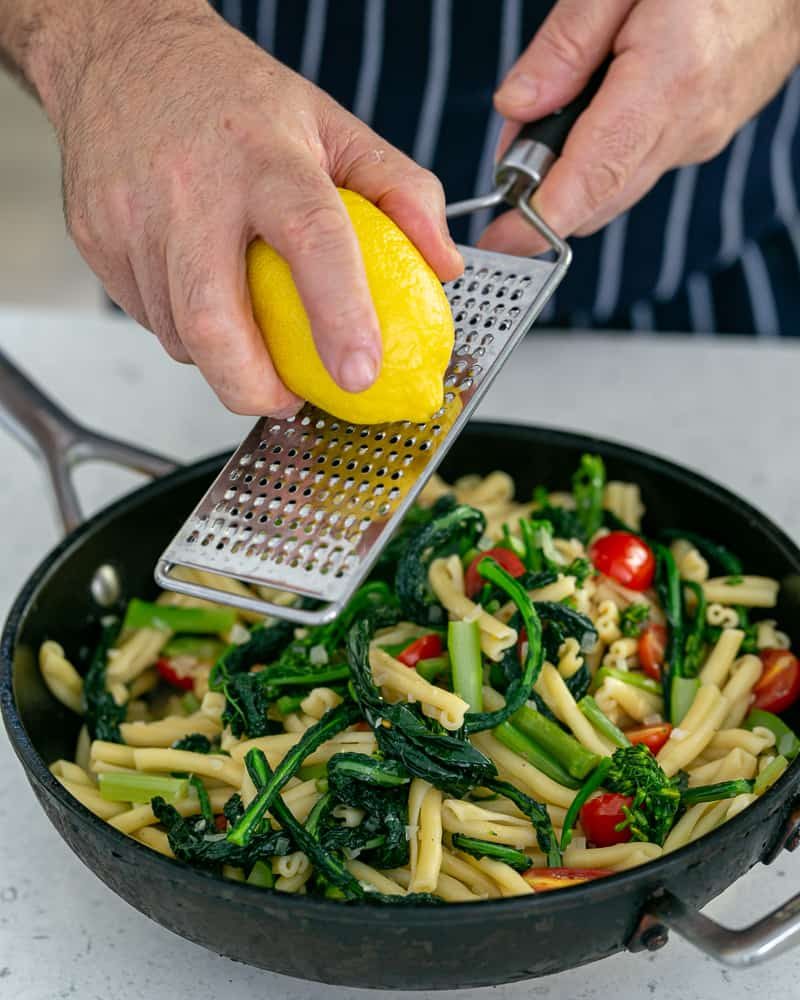 grating lemon zest over a pan filled with pasta.