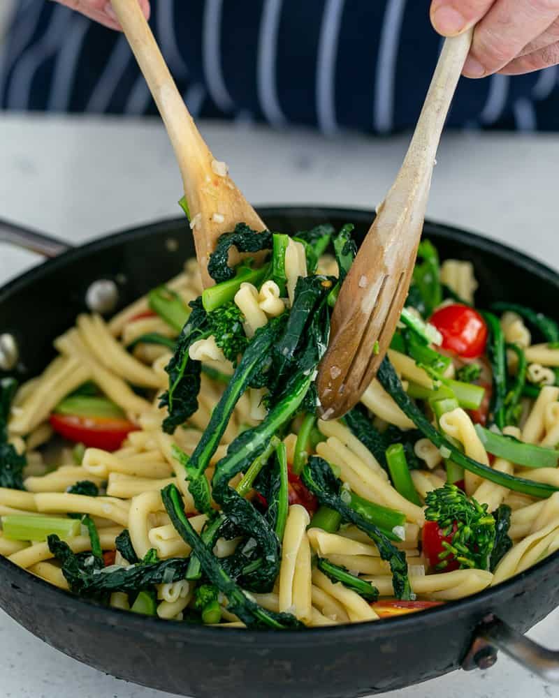 Tossing pasta in a pan with two wooden spoons