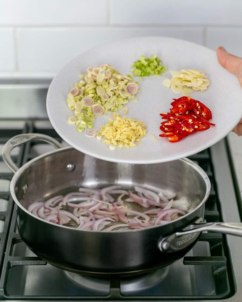 Searing sliced onions with other ingredients in a pan to make the coconut curry sauce