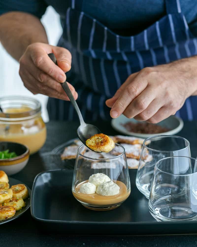 Adding caramelized banana slices on top of dulche de leche in glass