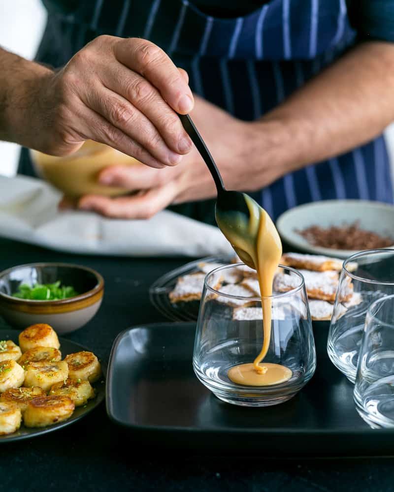 Adding a spoonful of the Dulche de leche at the bottom in the glass to assemble Dulce de Leche Verrine with Banana and whipped Cream