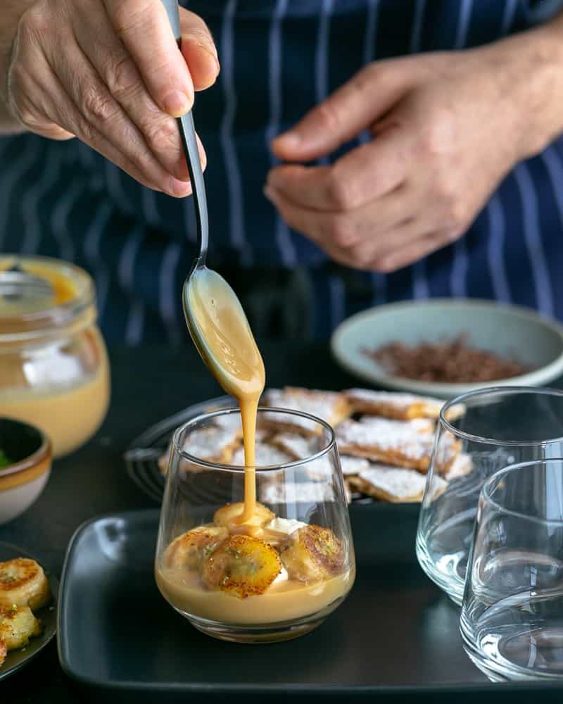 Adding a spoonful of the dulche de leche with a swirl on top of the caramelized bananas in glass