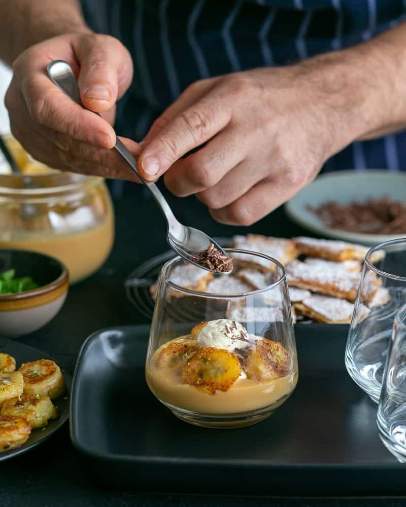 Adding shaved dark chocolate on Dulce de Leche Verrine with Banana and whipped Cream