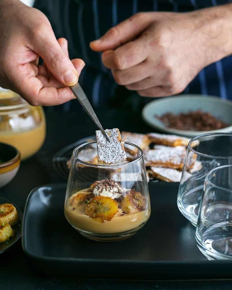 Adding puff pastry chard in different directions in the glass while assembling Dulce de Leche Verrine with Banana and whipped Cream