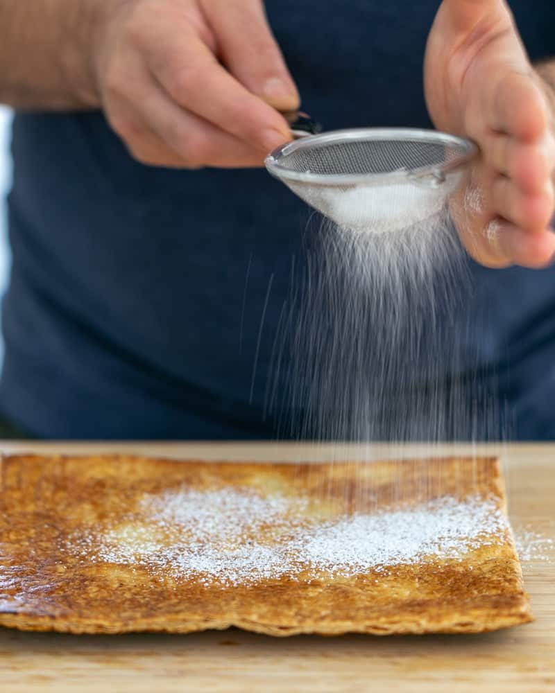 Dustying icing sugar on baked puff pastry for Dulce de Leche Verrine with Banana and whipped Cream