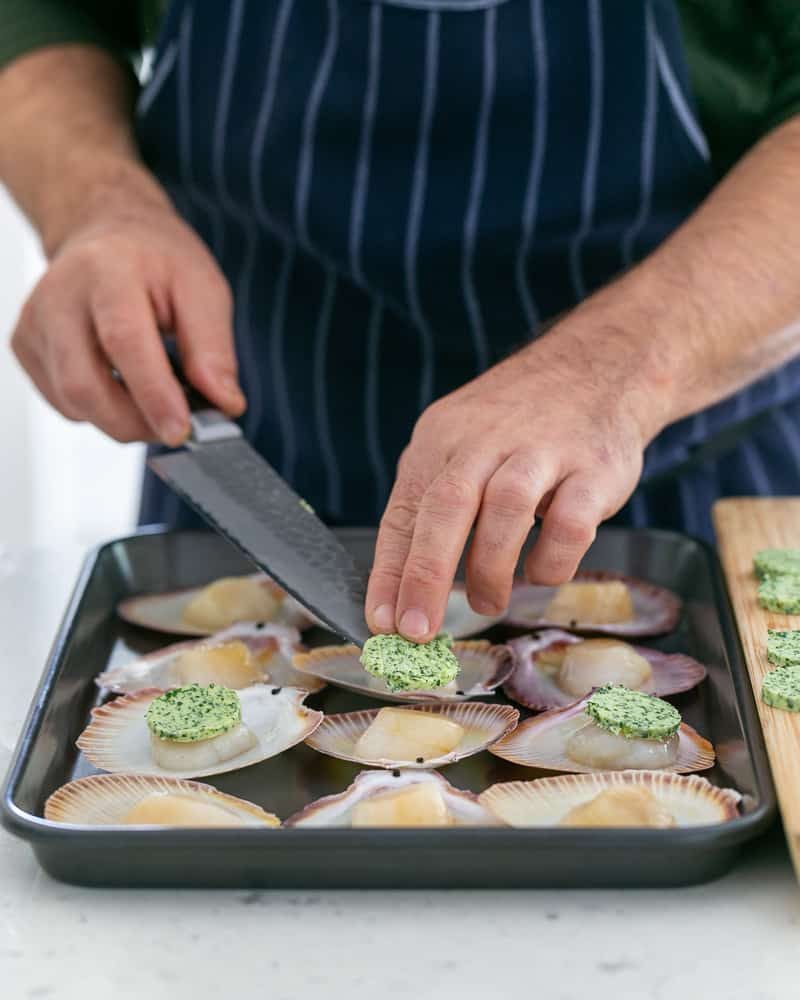 Adding garlic butter discs on top of scallops to be baked in the oven in their shell