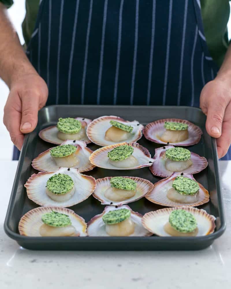 Adding garlic butter discs on top of scallops to be baked in the oven in their shell