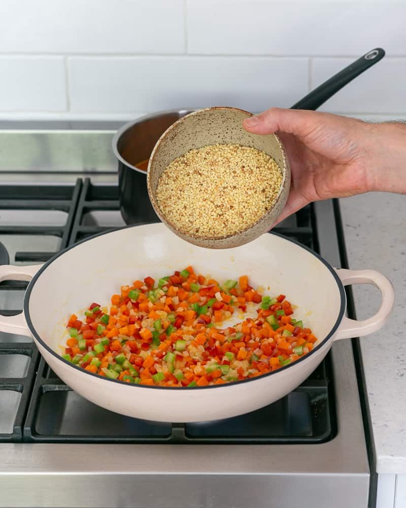 adding fregola sarda to a pot with sauteed vegetables